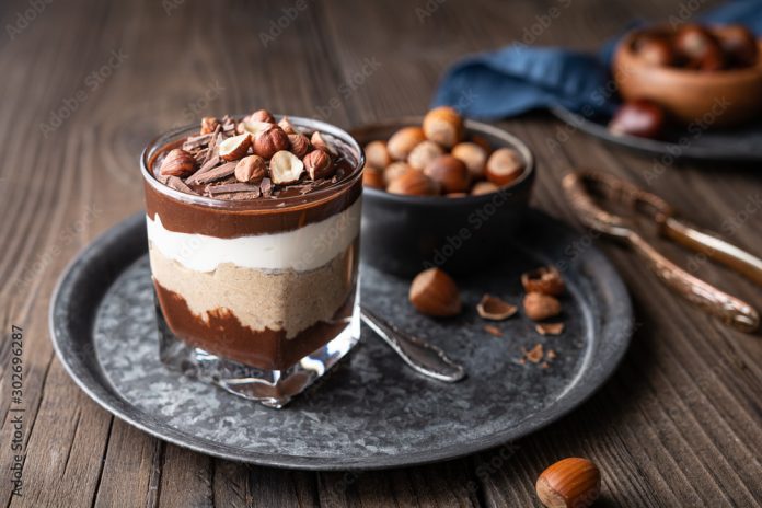 Layered dessert with chocolate mousse, cream cheese and whipped cream mixed with chestnut puree, topped with hazelnuts in a glass jar