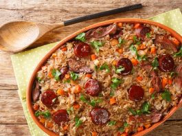Portuguese duck rice arroz de pato cooked with red wine, onion, carrot and chorizo close up in the baking dish on the wooden table. Horizontal top view from above