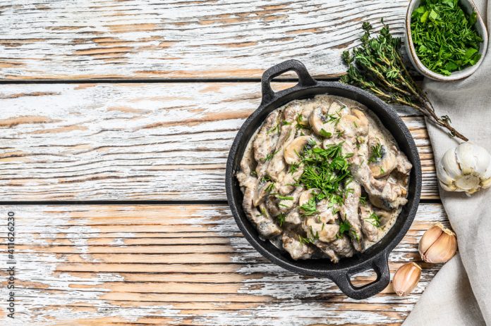 Beef stroganoff with mushrooms in frying pan. White background. Top view. Copy space
