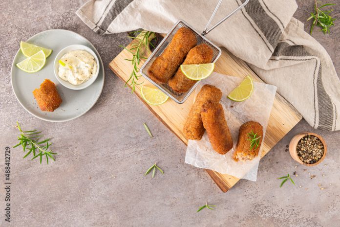 Meat croquets with garlic mayonnaise, lime slices to season and rosemary leaves on wooden table in a kitchen counter top.