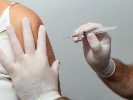 Mãos de médico ou enfermeiro aplicando vacina no braço de paciente.