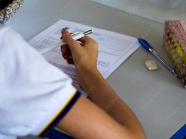 Student taking exam with school supplies on the table.